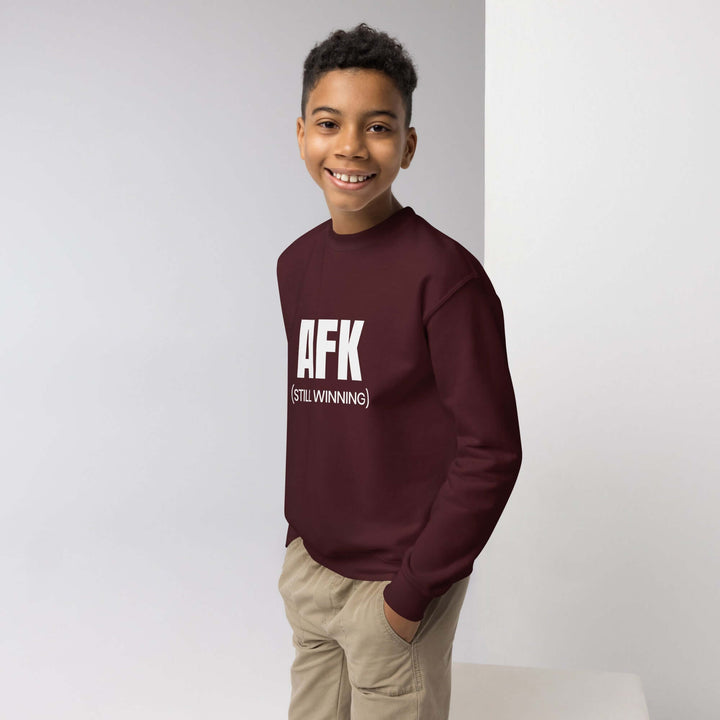 Smiling boy wearing the AFK youth crewneck sweatshirt in maroon, showcasing comfort and style for active kids.